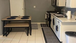Cocina compacta equipada con refrigerador, estufa, microondas y una pequeña mesa de comedor con taburetes.