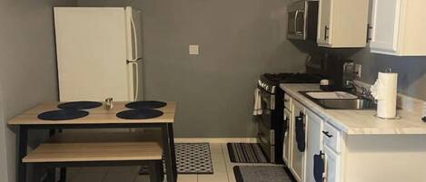 A compact kitchen with a refrigerator, stove, microwave, and a small dining table with stools.