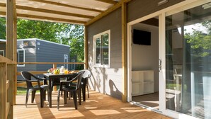 A covered outdoor area with a table and chairs, a glass door leading to a patio, and a view of a neighboring building.