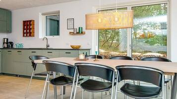 A modern kitchen with a dining area, featuring a large window, a hanging light fixture, and a view of the outdoors.