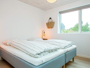 Quarto com cama, luminária de cabeceira, janela e cesta suspensa.