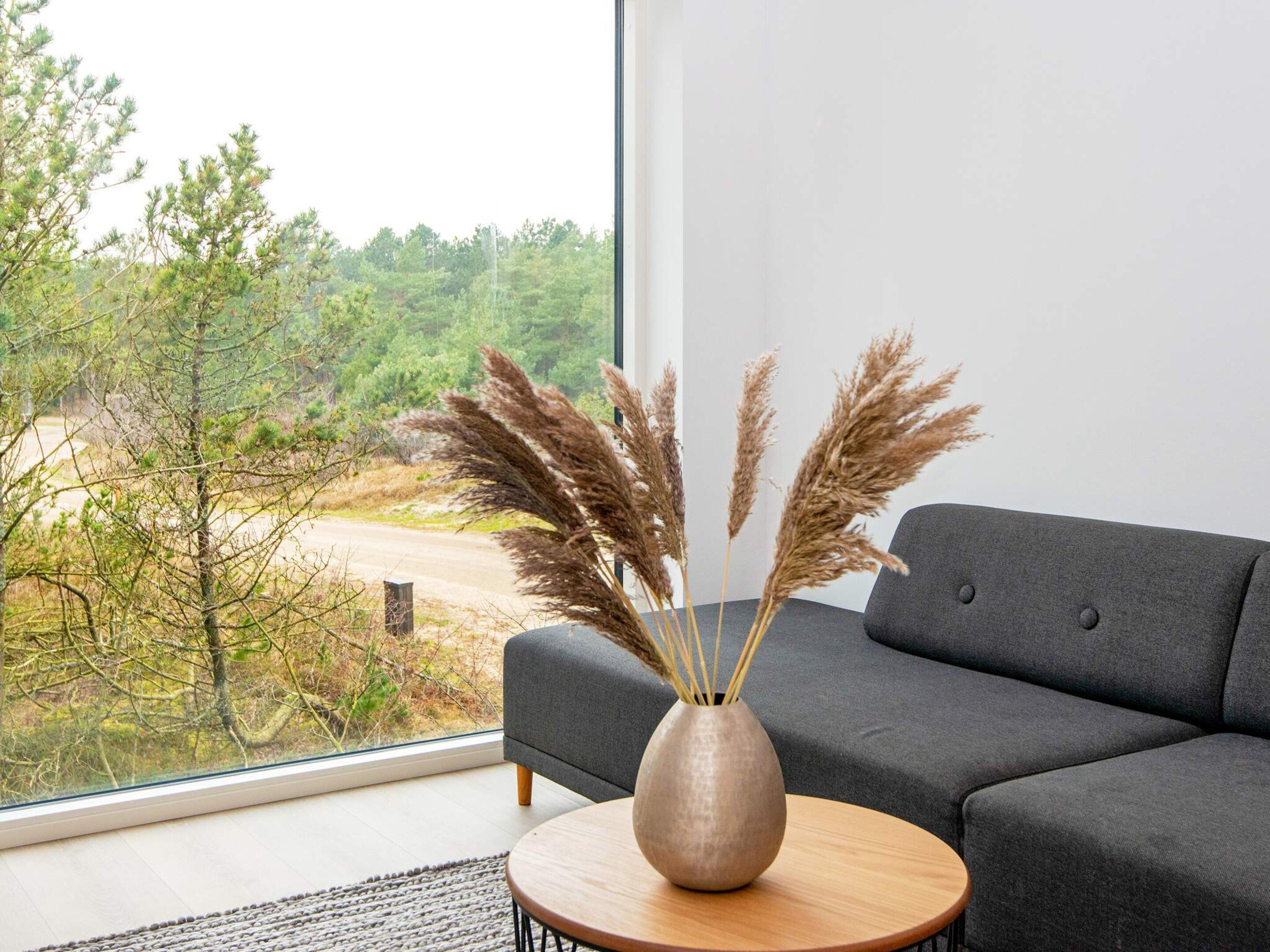 Ein modernes Wohnzimmer mit einem grauen Sofa, einem runden Couchtisch und einer Vase mit Pampasgras.