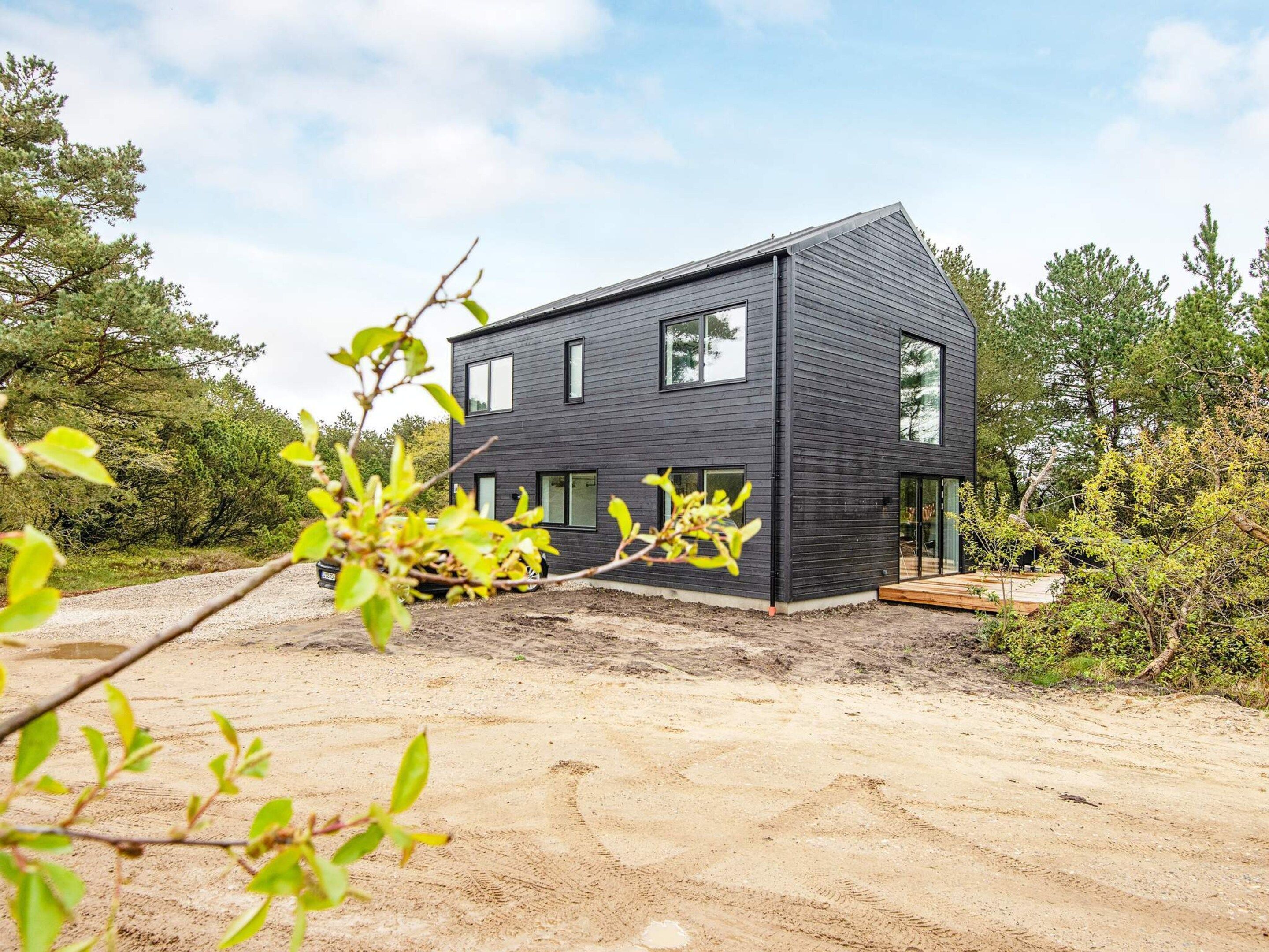 Ein modernes, zweistöckiges Haus mit dunkler Fassade, einer sichtbaren Garage und einer Schotterzufahrt.