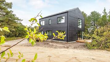 Ein modernes, zweistöckiges Haus mit dunkler Fassade, einer sichtbaren Garage und einer Schotterzufahrt.