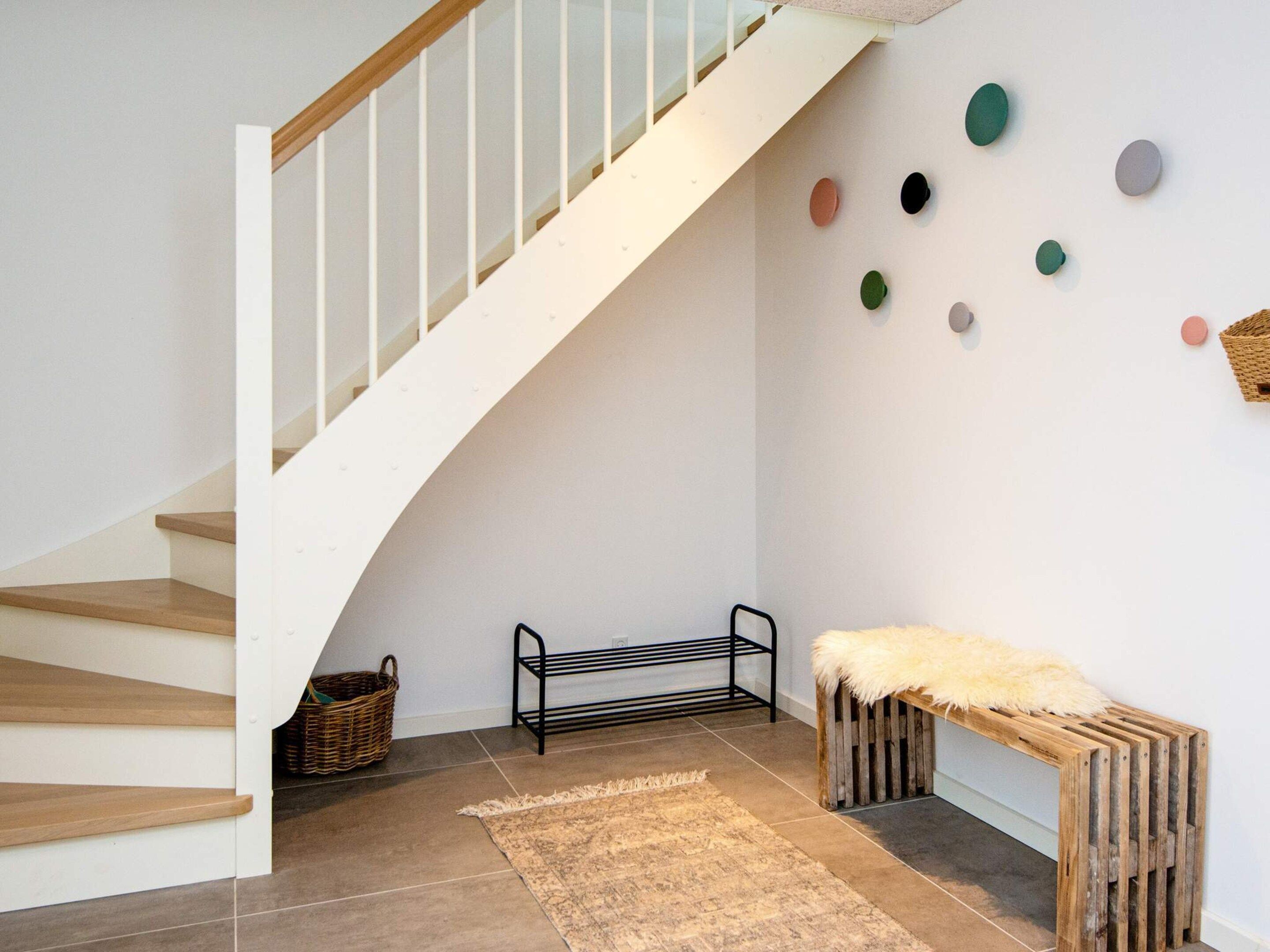 A staircase with a wooden handrail and white walls, a bench with a fur throw, a metal rack, and a patterned rug.