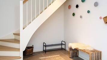 A staircase with a wooden handrail and white walls, a bench with a fur throw, a metal rack, and a patterned rug.
