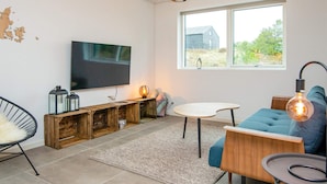 Un salon moderne doté d’un téléviseur à écran plat, de meubles de rangement en bois, d’un canapé bleu et d’une grande fenêtre offrant une vue sur la verdure.