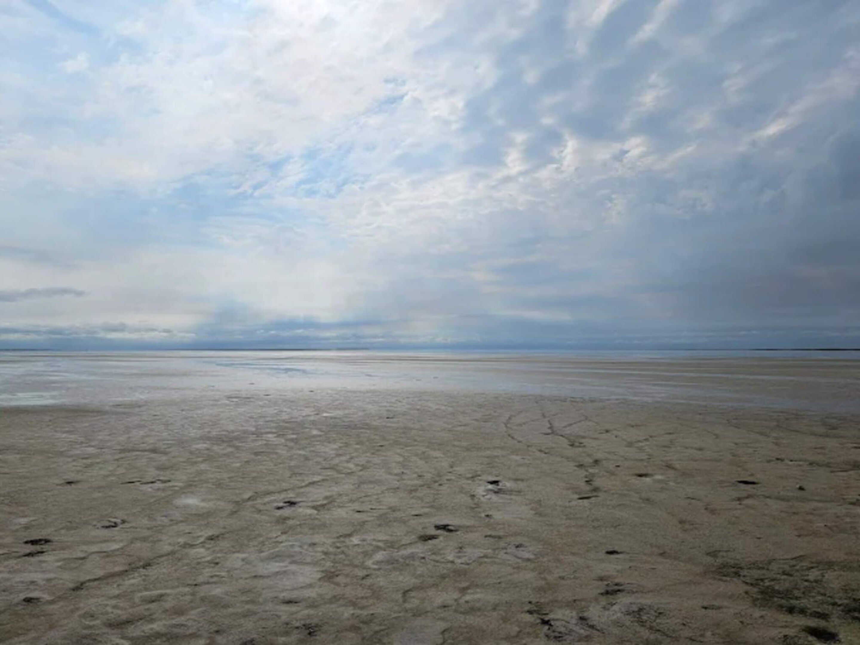 A wide, flat beach with a cloudy sky.