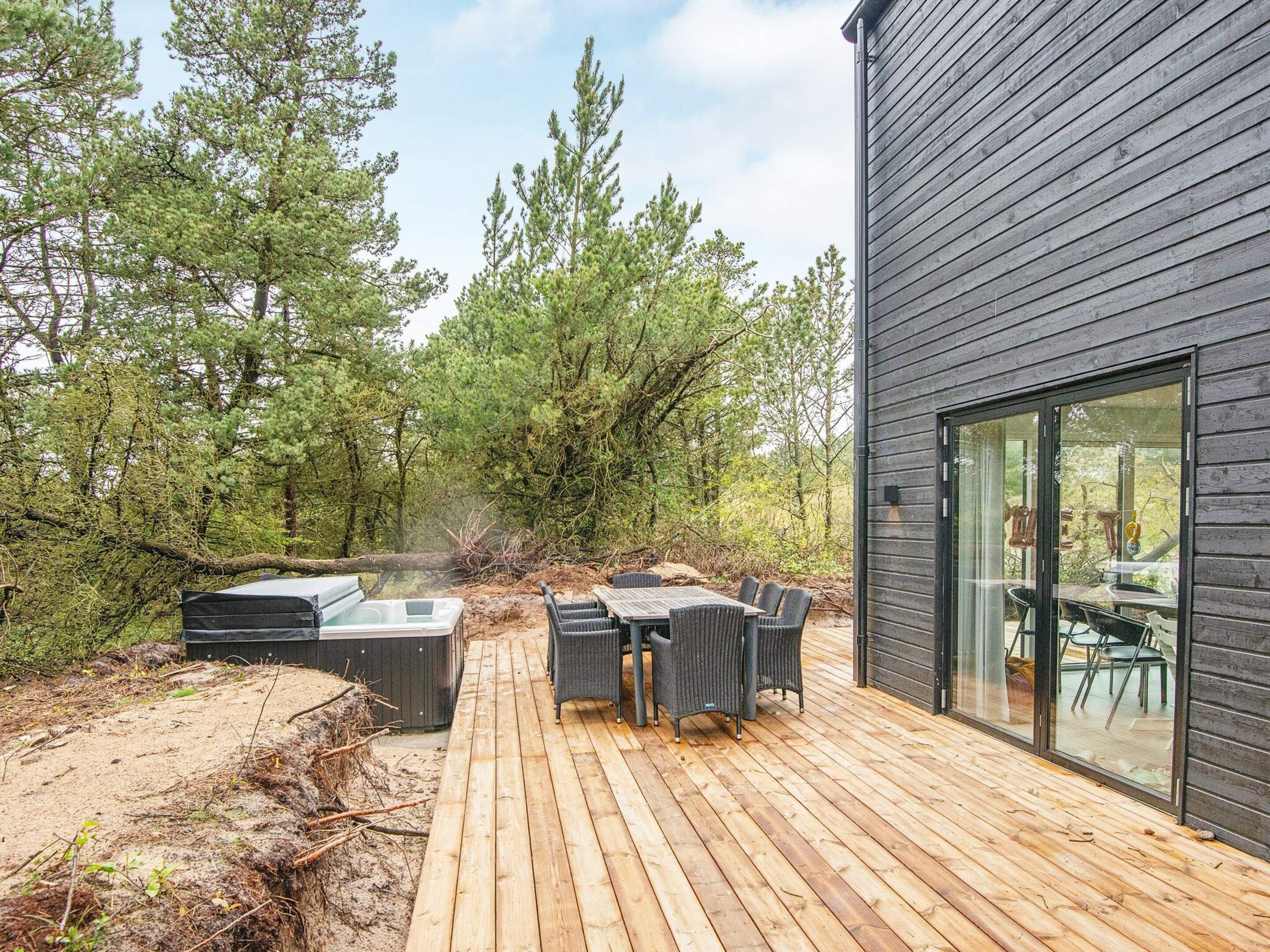 Une terrasse en bois, agréée de meubles d’extérieur, et entourée d’arbres.