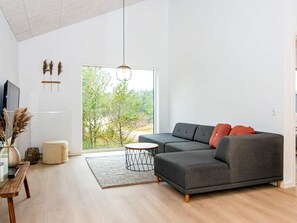 Uma sala de estar moderna com um sofá modular, uma mesa de centro redonda e uma grande janela com vista para árvores.