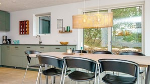 Une cuisine moderne avec un coin repas, dotée d’une grande fenêtre, d’un luminaire suspendu et offrant une vue sur l’extérieur.