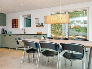 A modern kitchen with a dining area, featuring a large window, a hanging light fixture, and a view of the outdoors.