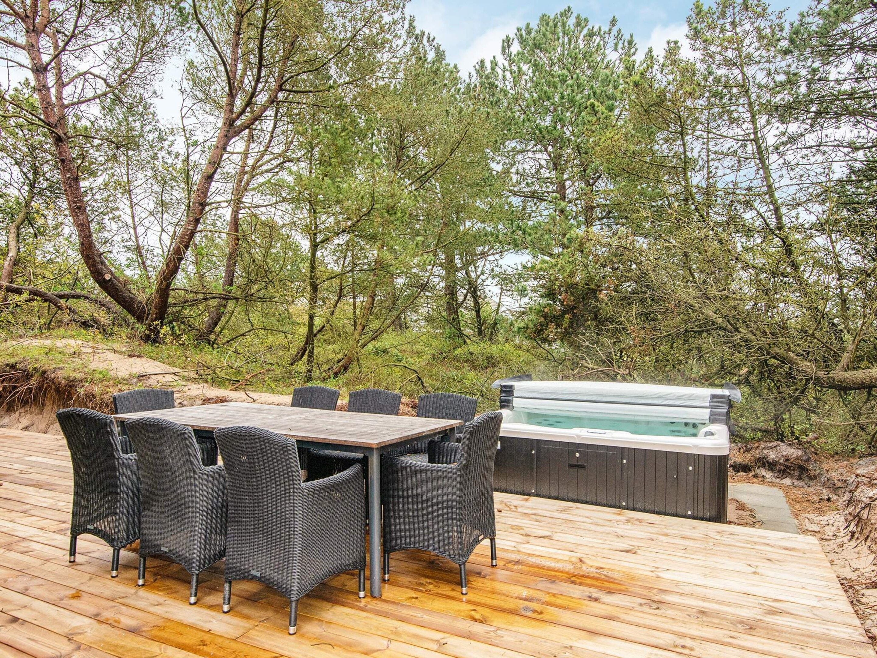 Eine Terrasse im Freien mit Holztisch und Korbstühlen, umgeben von Bäumen und einem Whirlpool.