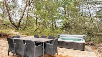 Eine Terrasse im Freien mit Holztisch und Korbstühlen, umgeben von Bäumen und einem Whirlpool.