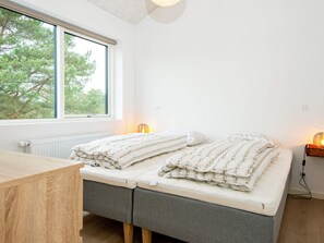 A bedroom with a bed, a desk, a window, and a nightstand with a lamp.