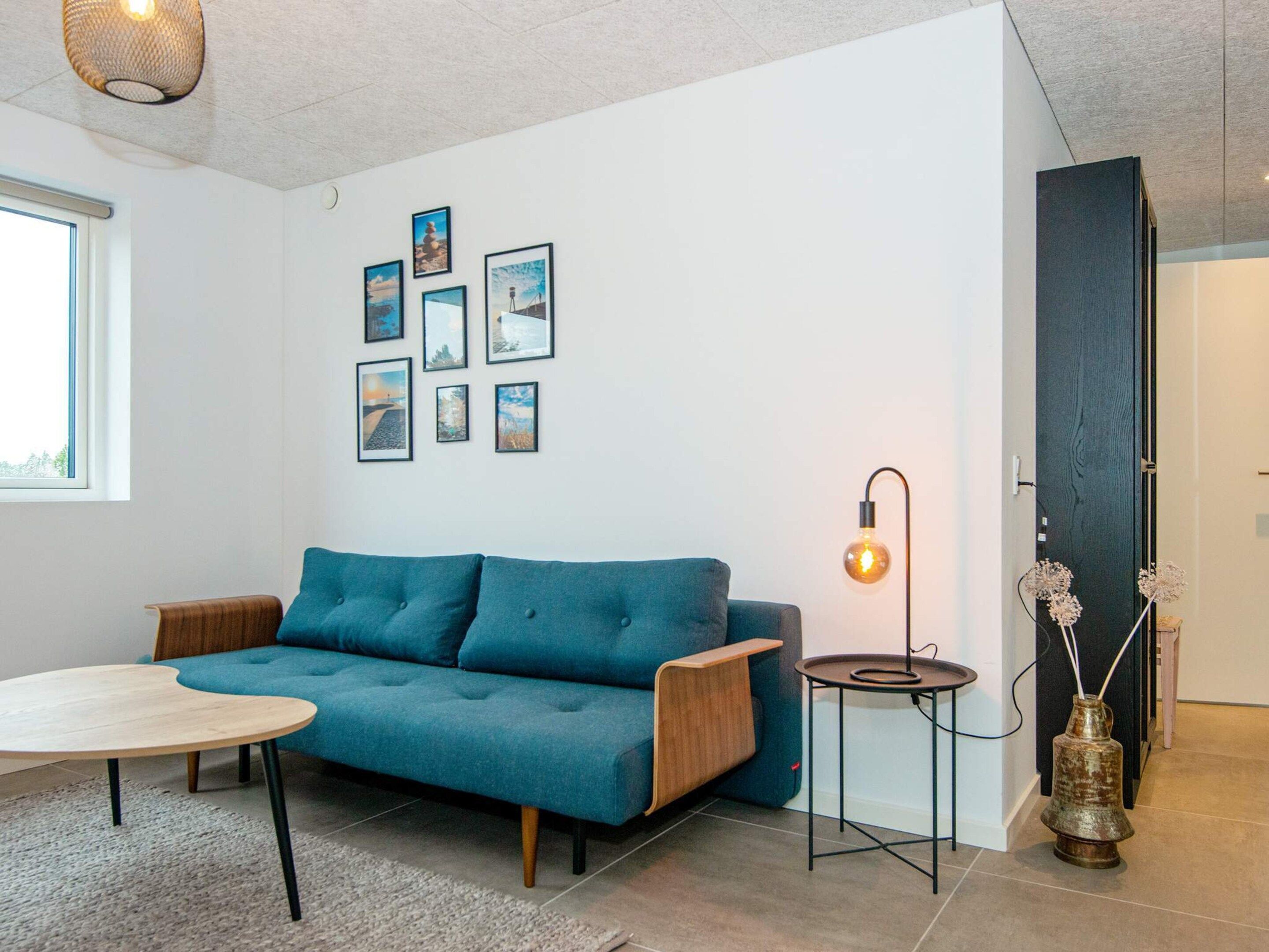 A modern living room with a blue sofa, a round coffee table, a wall-mounted light fixture, and a series of framed pictures.