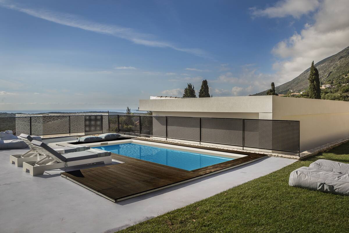 A modern outdoor pool area with a wooden deck, lounge chairs, and a view of the mountains.