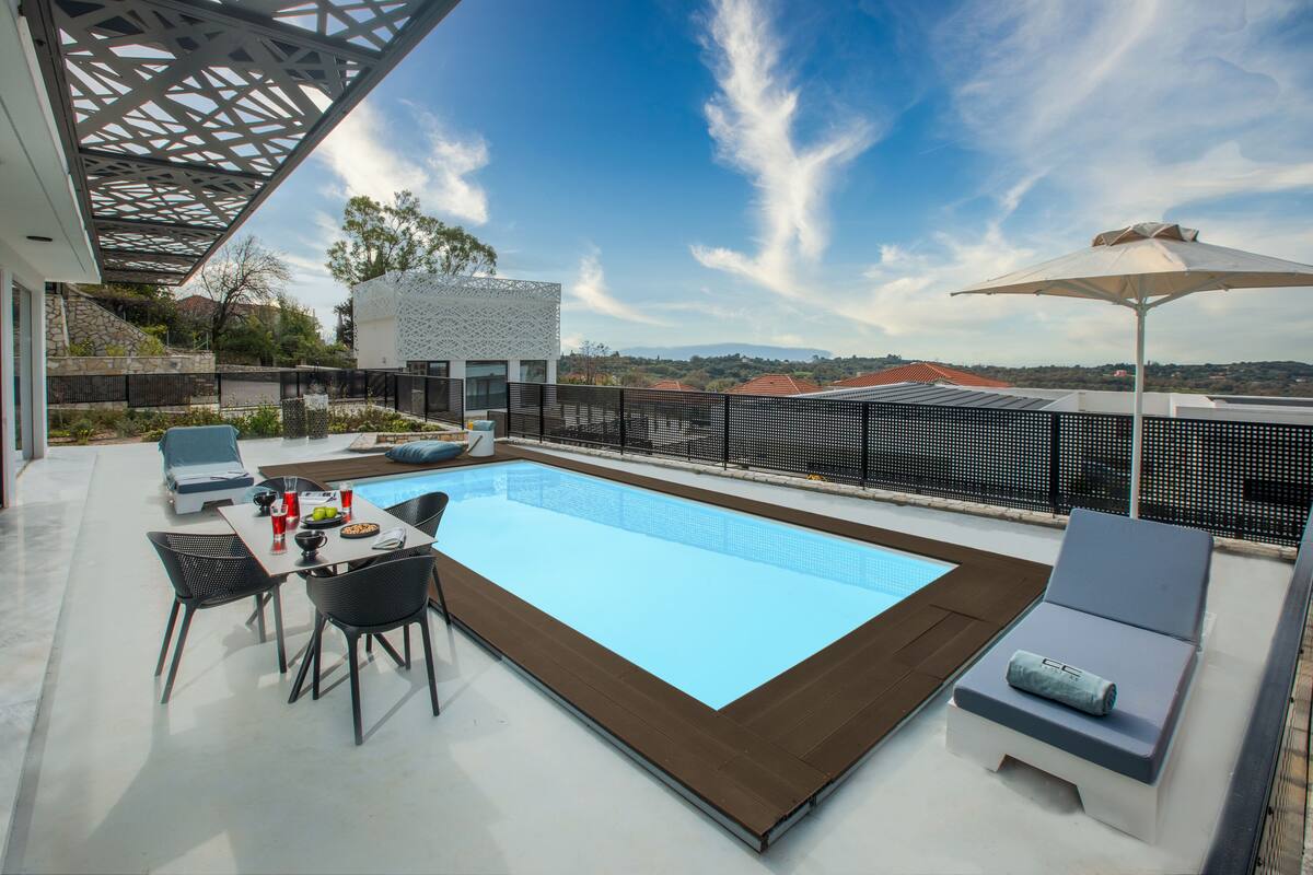 A rooftop pool area with a clear view of the cityscape, including a modern building and distant mountains.