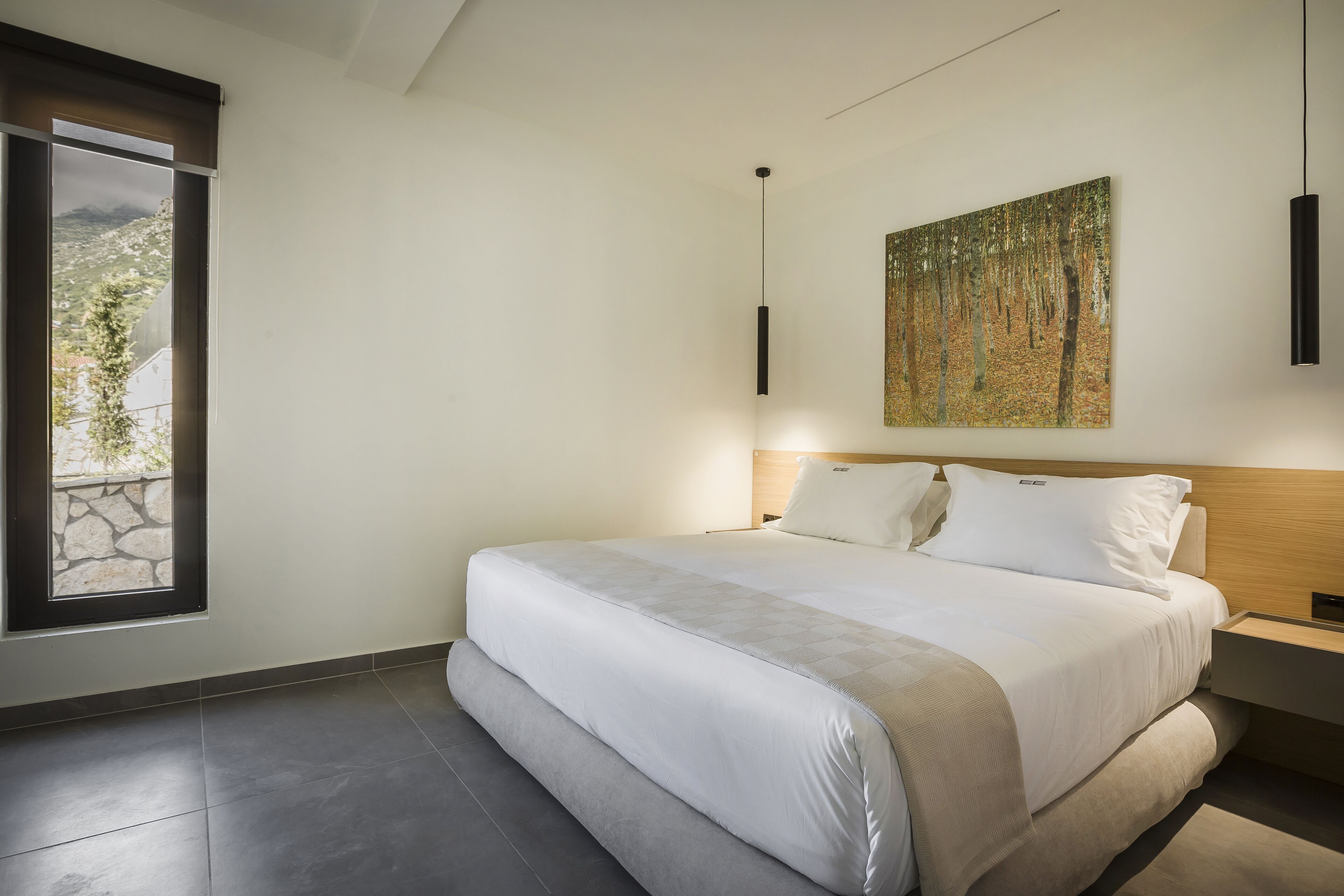 A modern bedroom with a large bed, a painting on the wall, and a window with a view.