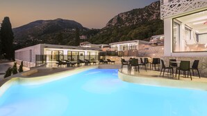 Un hotel moderno con piscina, sillones de descanso y montañas al fondo.