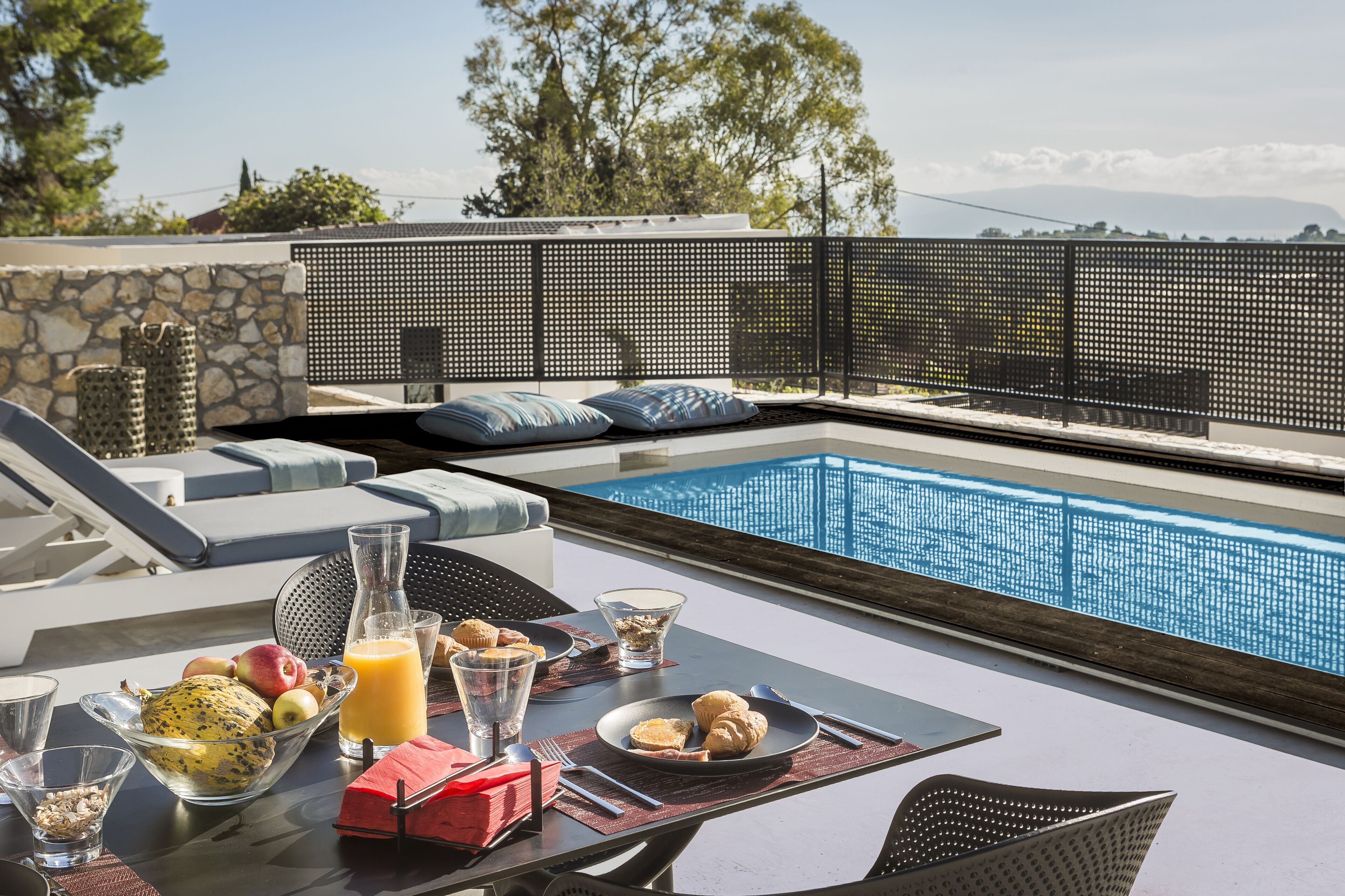 A poolside breakfast setup with a table, chairs, and a view of the pool and surrounding landscape.