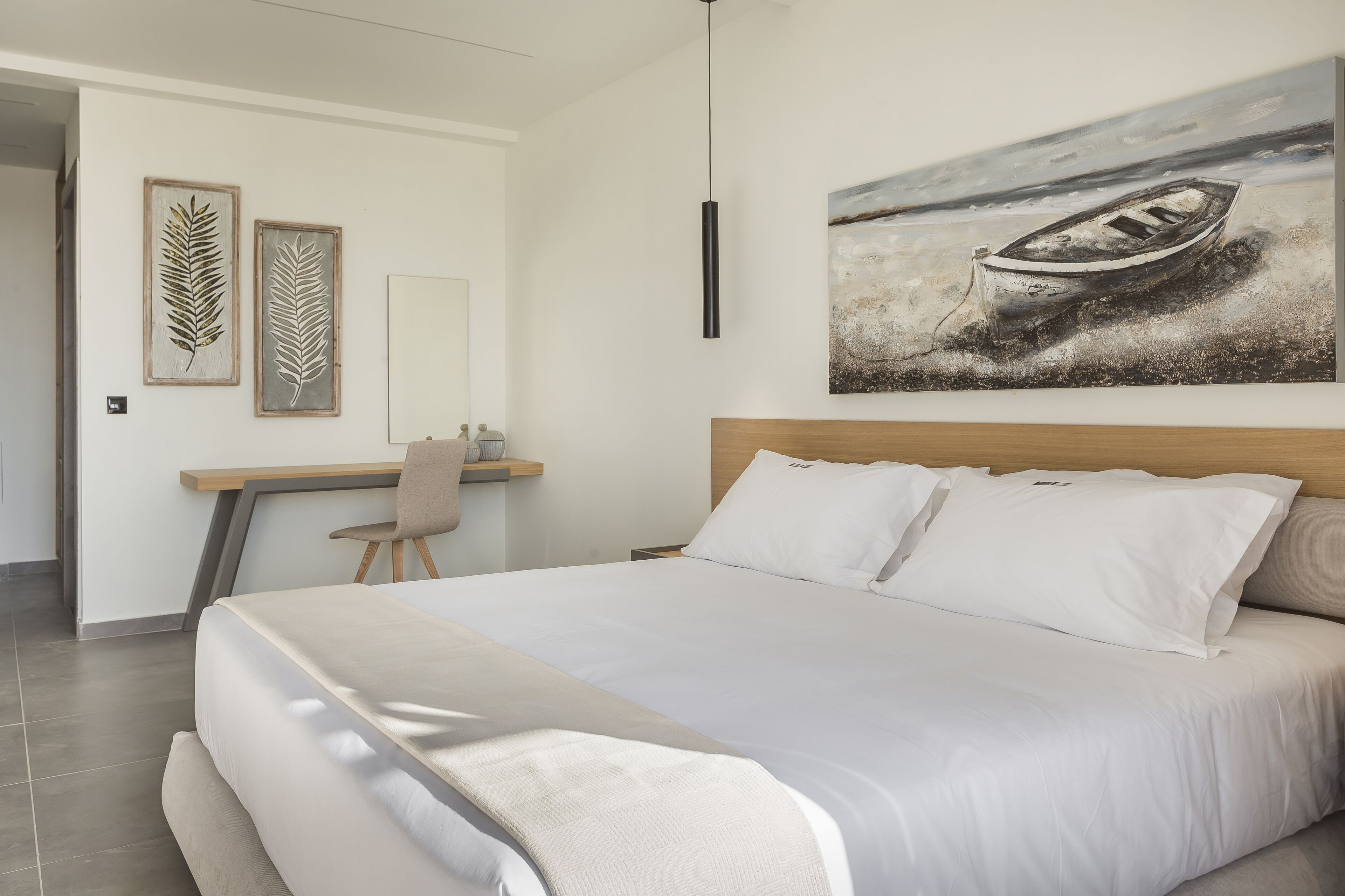 A modern hotel room with a large bed, a desk, and a painting of a boat on the wall.