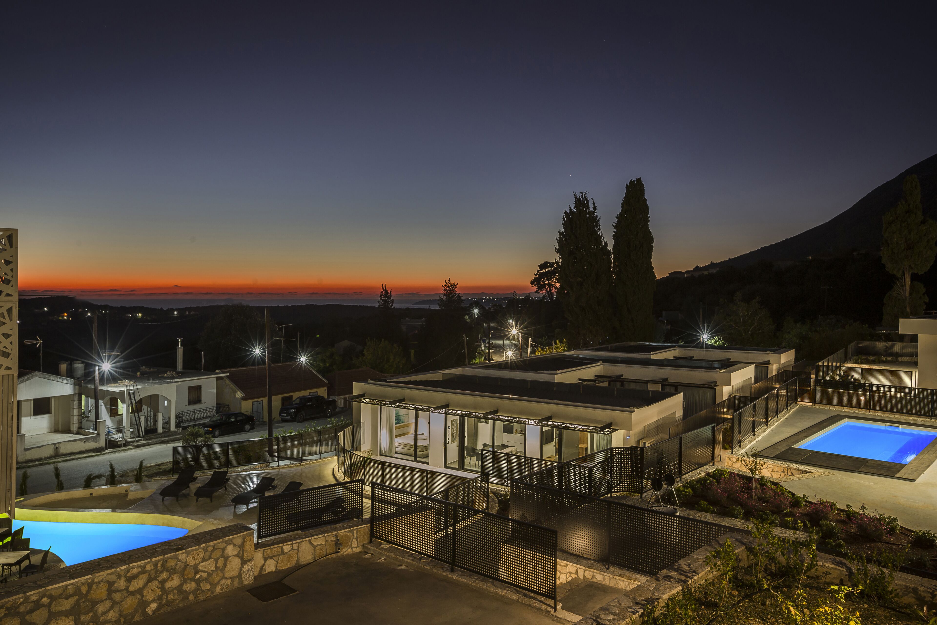 A modern villa with a swimming pool, outdoor seating, and a view of the sunset.