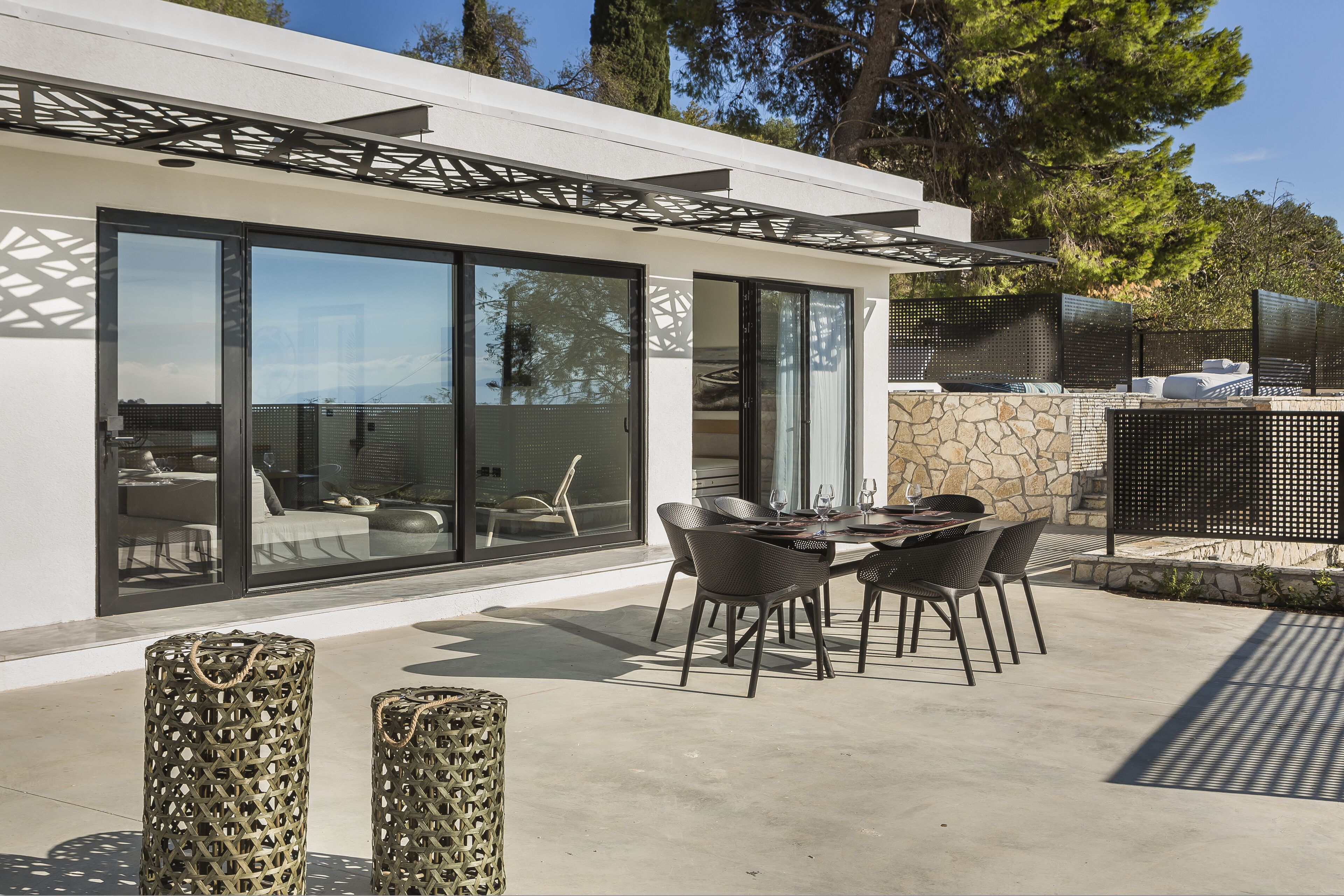 A modern outdoor patio with a dining table and chairs, a stone wall, and a glass door leading to an interior space.