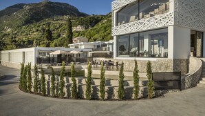 Un edificio moderno con fachada de vidrio, zona de estar al aire libre y vistas a un paisaje montañoso.