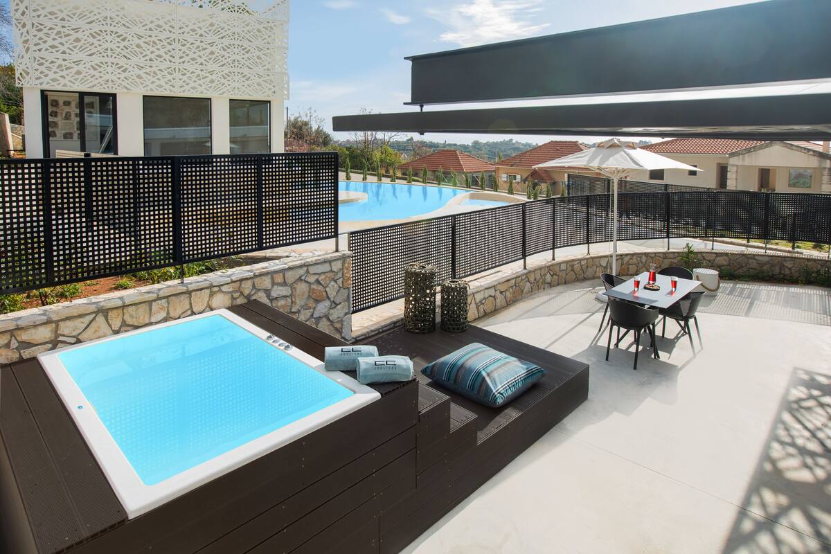 A modern outdoor pool area with a hot tub, seating, and a covered patio.