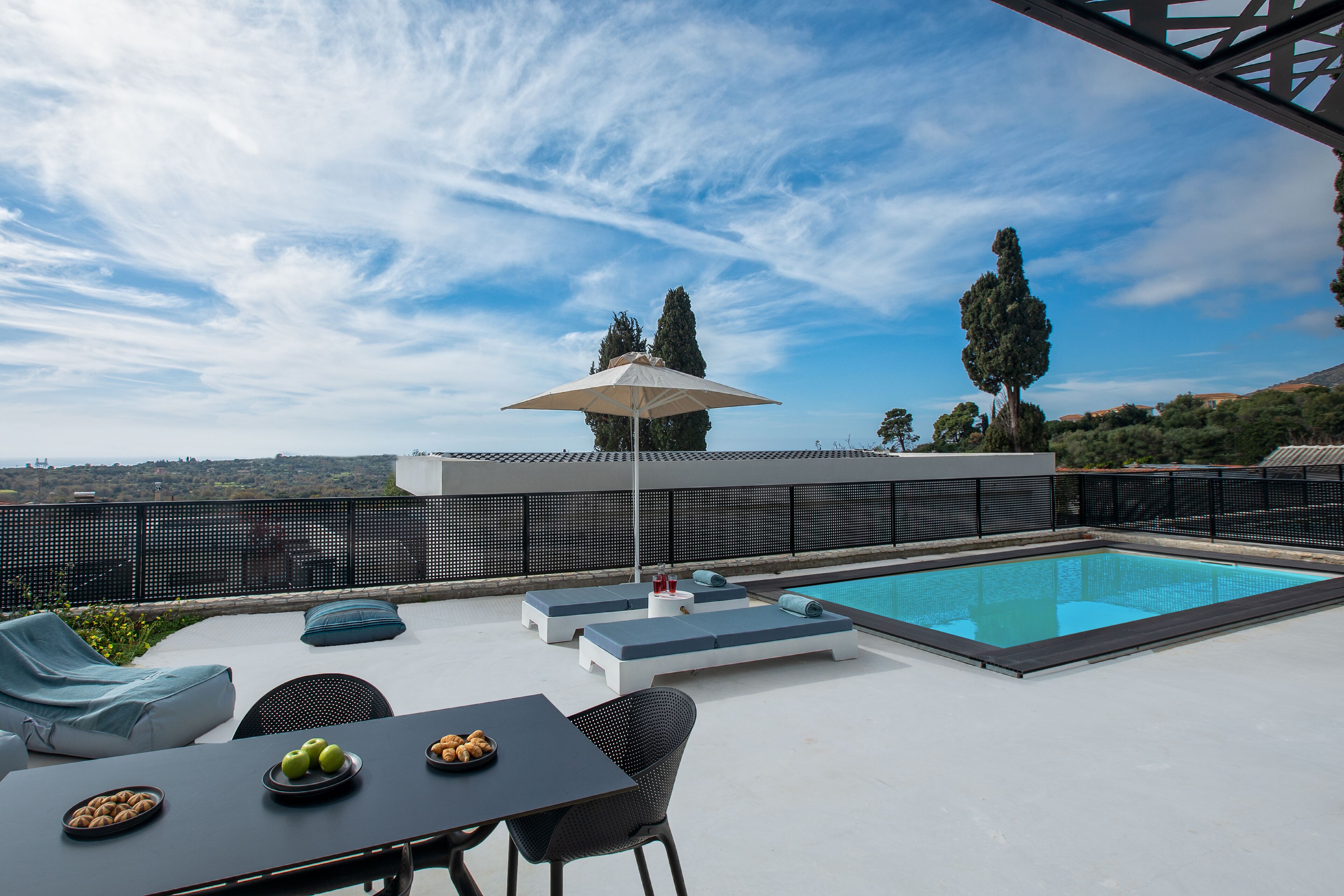 Area piscina sul tetto con lettini, un tavolo con frutta e vista sulla città.