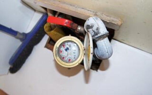 Un compteur d’eau, un tuyau rouge et un tuyau blanc dans un espace technique.