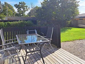 A deck with a glass table and chairs, surrounded by a wooden fence and a grassy yard. - 6 Person Holiday Home in Hadsund (Hadsund)