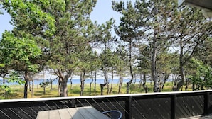 A wooden deck with a table and chairs, overlooking a beach with trees and a clear sky. - 6 Person Holiday Home in Sjaellands Odde-by Traum (Sjællands Odde)
