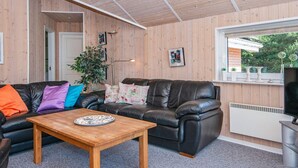 Ein gemütliches Wohnzimmer mit einer schwarzen Ledersofa, einem Holztisch und einem großen Fenster mit Blick auf Grün.
