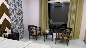 Ein Hotelzimmer mit einem Bett, zwei Holzstühlen, einem kleinen Tisch, einem Nachttischtelefon und einem Fenster mit Vorhängen.
