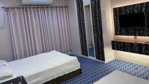 Ein Hotelzimmer mit Bett, Wandfernseher, Klimaanlage und Duschbereich mit Vorhängen.