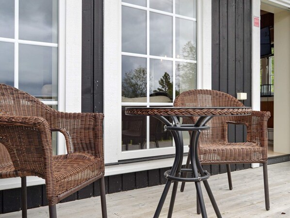 A wicker chair and table set on a wooden deck in front of a building with large windows. - 4 Star Holiday Home in Rauland (Vinje)