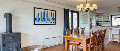 A dining area with a wooden table and chairs, a black stove, and a painting of sailboats on the wall.