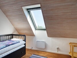 Un dormitorio con techo inclinado, ventana, cama, radiador y suelo de madera.