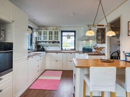 A kitchen with white cabinets, a wooden countertop, a pink rug, and pendant lights.