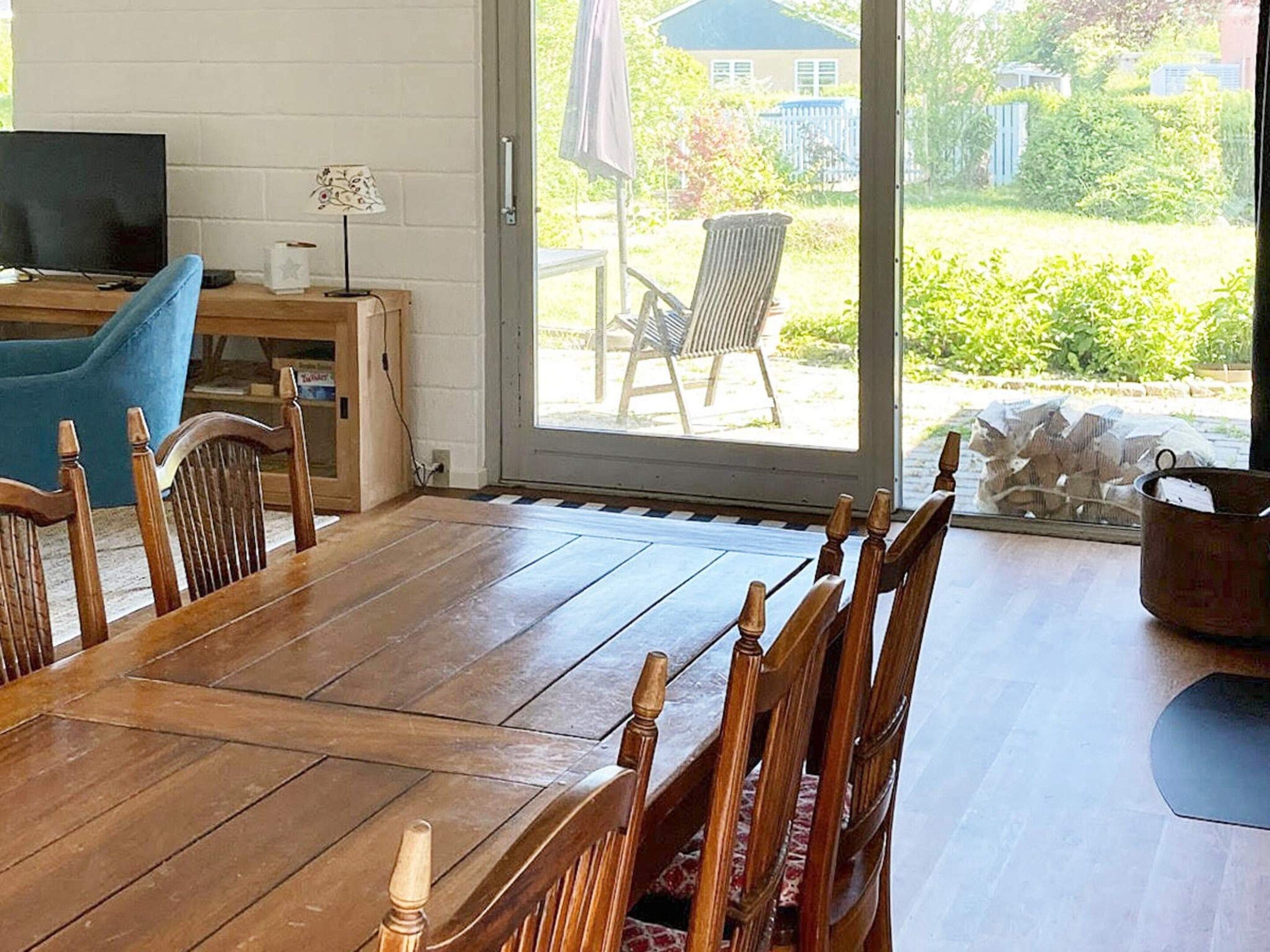 A dining area with a wooden table and chairs, a television, and a view of a garden through a glass door.