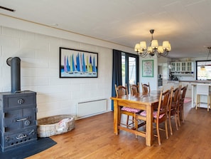 A dining area with a wooden table and chairs, a black stove, and a painting of sailboats on the wall. - 7 Person Holiday Home in Nakskov (Nakskov)