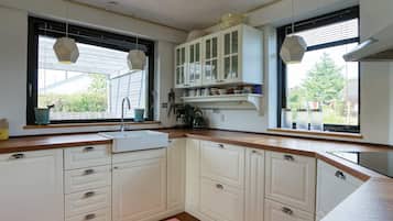 A kitchen with white cabinets, a wooden countertop, a sink, and a window with a view of greenery.