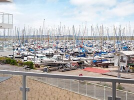Un puerto deportivo con numerosas embarcaciones amarradas, una pequeña estructura con techo y una zona arenosa en primer plano.