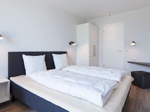 A modern bedroom with a large bed, a nightstand, a wardrobe, and two wall-mounted lamps. - 5 Star Holiday Home in Wendtorf (Wendtorf)