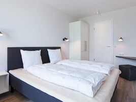 Un dormitorio moderno con una cama grande, una mesita de noche, un armario y dos lámparas de pared.