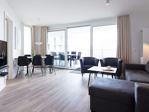 A modern living room with a dining area, large windows, and a flat-screen TV.