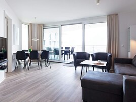 Ein modernes Wohnzimmer mit Essbereich, großen Fenstern und einem Flachbildfernseher.