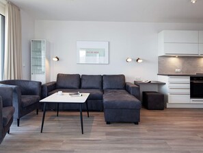 A modern living room with a sectional sofa, a coffee table, and a kitchen area with a built-in oven.